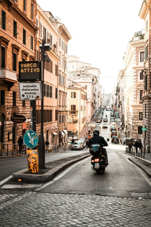 Man riding a scooter through the streets of Rome